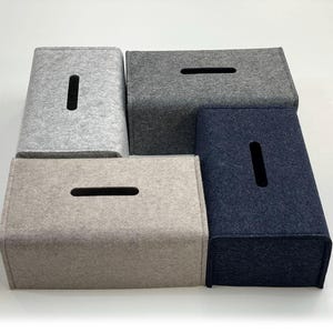 以下が含まれることがあります： グレーとネイビーブルーの様々な色合いの、長方形のティッシュボックスカバー4つのコレクション。各カバーには上部に長方形の開口部があります。カバーはフェルトのような素材で作られています。