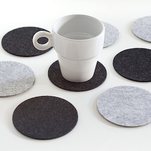 May include: A white ceramic mug sits on a gray and black felt coaster. The coaster is surrounded by other gray and black felt coasters.