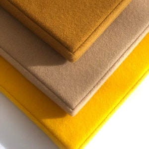 May include: Three fabric squares stacked on top of each other. The top square is a mustard yellow color, the middle square is a light brown color, and the bottom square is a bright yellow color.