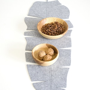 May include: Two wooden bowls on a gray felt leaf-shaped placemat. One bowl is filled with almonds, the other with walnuts.