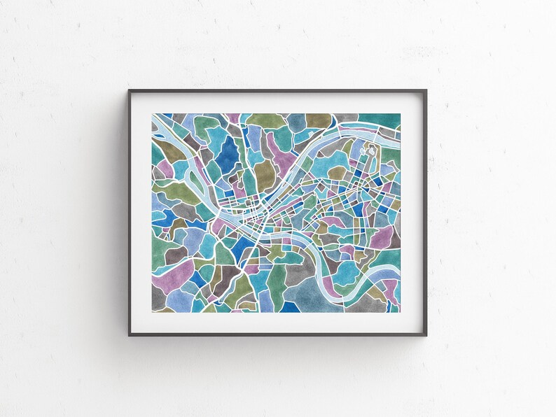 May include: A colorful watercolor map of a city with a river winding through it. The map is framed in a black frame and is hanging on a white wall.