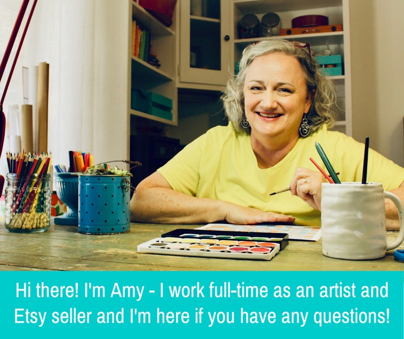 May include: A woman sits at a table with art supplies, including colored pencils, markers, and watercolors. She is smiling and holding a paintbrush. The text on the image reads "Hi there! I'm Amy - I work full-time as an artist and Etsy seller and I'm here if you have any questions!"