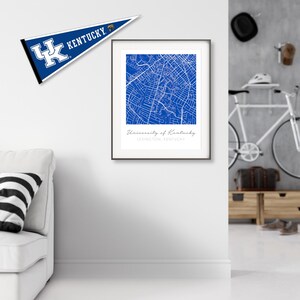 May include: A framed print of a blue map of the University of Kentucky campus in Lexington, Kentucky. The map is surrounded by a white border and a black frame. The print is hanging on a white wall.