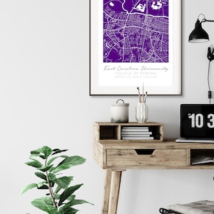 May include: A purple and white map print of East Carolina University College of Nursing in Greenville, North Carolina. The print is framed in a black frame and is hanging on a white wall.