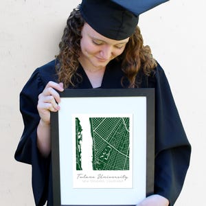 May include: A framed print of a green map of Tulane University in New Orleans, Louisiana. The print is held by a person wearing a black graduation cap and gown.
