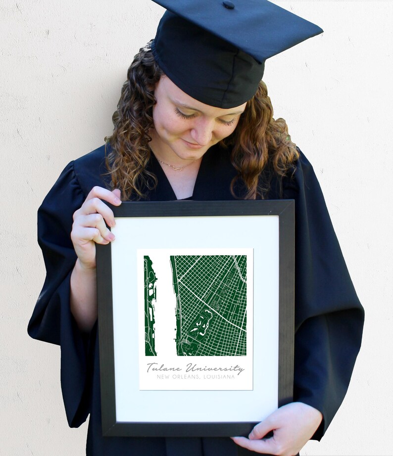 May include: A framed print of a green map of Tulane University in New Orleans, Louisiana. The print is held by a person wearing a black graduation cap and gown.