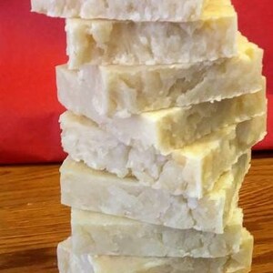 May include: A stack of 10 rectangular bars of white soap. The soap is stacked on a wooden surface.