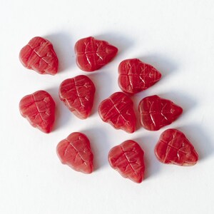 May include: Ten red leaf-shaped gummy sweets on a white surface.