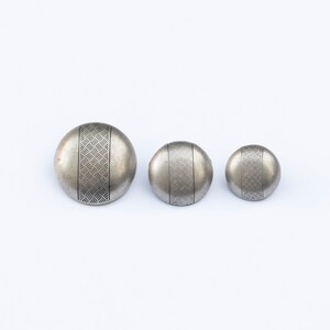 May include: Three silver metal buttons with a geometric pattern. The buttons are different sizes.