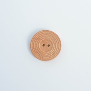 Puede incluir: Un botón redondo de madera con círculos concéntricos y dos agujeros en el centro.