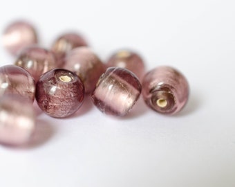Op de afbeelding: Een groep van iriserende paarse glazen kralen met een metallic glans. De kralen zijn rond en hebben een gat in het midden om te rijgen.