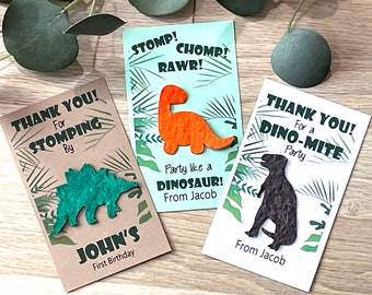 May include: Three thank you cards with dinosaur cutouts. The cards are brown, white, and light blue with green foliage designs. The text on the cards reads "Thank You! For Stomping By John's First Birthday", "Thank You! For a Dino-Mite Party", and "Stomp! Chomp! Rawr! Party like a Dinosaur! From Jacob".