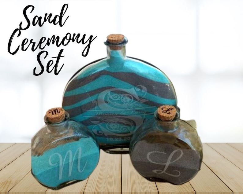 May include: Sand ceremony set with three glass bottles. The bottles are decorated with black and teal stripes and have cork tops. The bottles are labeled with the letters "M" and "L".