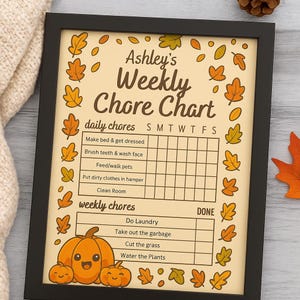 May include: A framed "Ashley's Weekly Chore Chart" with a fall theme. The chart features daily and weekly chores, with a pumpkin graphic at the bottom. The frame is black, and the background is tan with orange and yellow leaf accents.