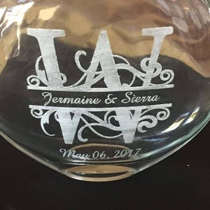 May include: A clear glass bottle with a heart-shaped base, engraved with the initials "J A" and the names "Jermaine & Sierra" and the date "May 06, 2017".