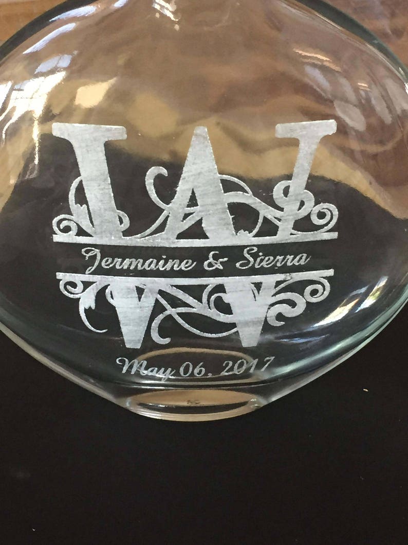 May include: A clear glass bottle with a heart-shaped base, engraved with the initials "J A" and the names "Jermaine & Sierra" and the date "May 06, 2017".
