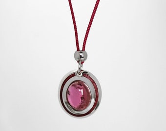 May include: A silver pendant necklace with a pink glass stone set in a double circle design. The necklace is on a red cord.