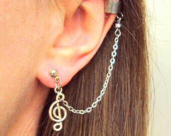 May include: Silver-toned ear cuff and earring set. The earring features a treble clef charm and a small stud. A delicate chain connects the earring to the ear cuff, which wraps around the upper ear. The jewelry is worn on a person's ear.