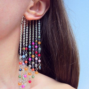 May include: A silver ear cuff with multiple strands of chain and colorful beads hanging down. The beads are in a rainbow pattern.