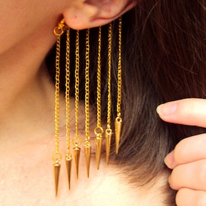 May include: Gold ear cuff with multiple dangling chains ending in sharp, pointed tips.