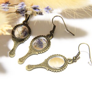 May include: A pair of antique-style bronze earrings with small oval mirrors featuring pressed flowers. The mirrors have a scalloped edge and the earrings have a hook closure.