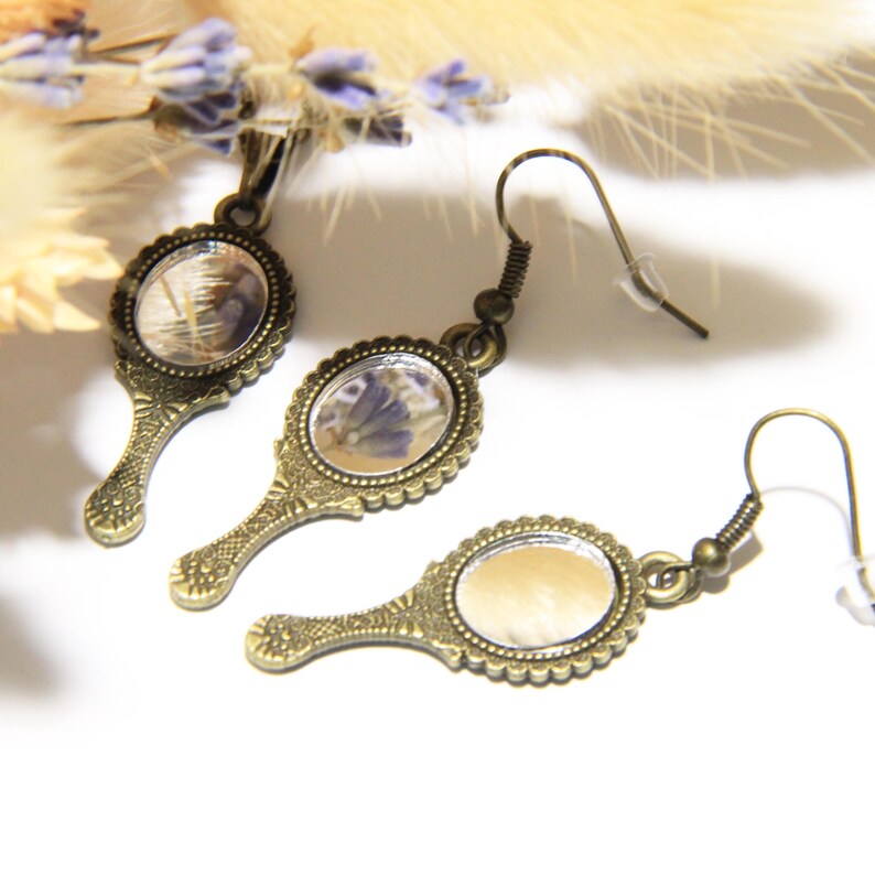 May include: A pair of antique-style bronze earrings with small oval mirrors featuring pressed flowers. The mirrors have a scalloped edge and the earrings have a hook closure.