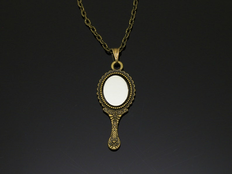 May include: A gold-toned necklace with a vintage-style hand mirror pendant. The mirror has a detailed ornate frame and a round reflective surface.