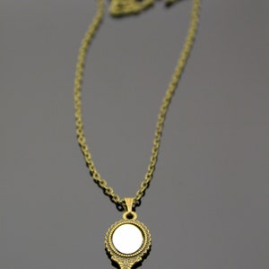 May include: A gold-toned necklace with a vintage-style hand mirror pendant. The mirror has a round shape and an ornate frame.