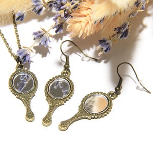 May include: A set of antique gold-toned hand mirror earrings and a necklace. The mirrors are round and have a beaded frame. The earrings have a hook closure. The necklace has a chain and a pendant.