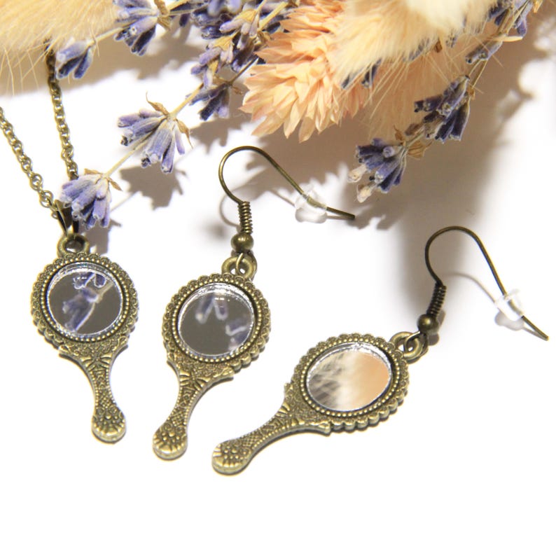May include: A set of antique gold-toned hand mirror earrings and a necklace. The mirrors are round and have a beaded frame. The earrings have a hook closure. The necklace has a chain and a pendant.