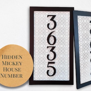 May include: Two rectangular house number signs with the number 3635 in black. The background has a white and gray pattern. One sign has a dark brown frame, the other has a black frame. A round sticker with the text "Hidden Mickey House Number" is in the lower left.