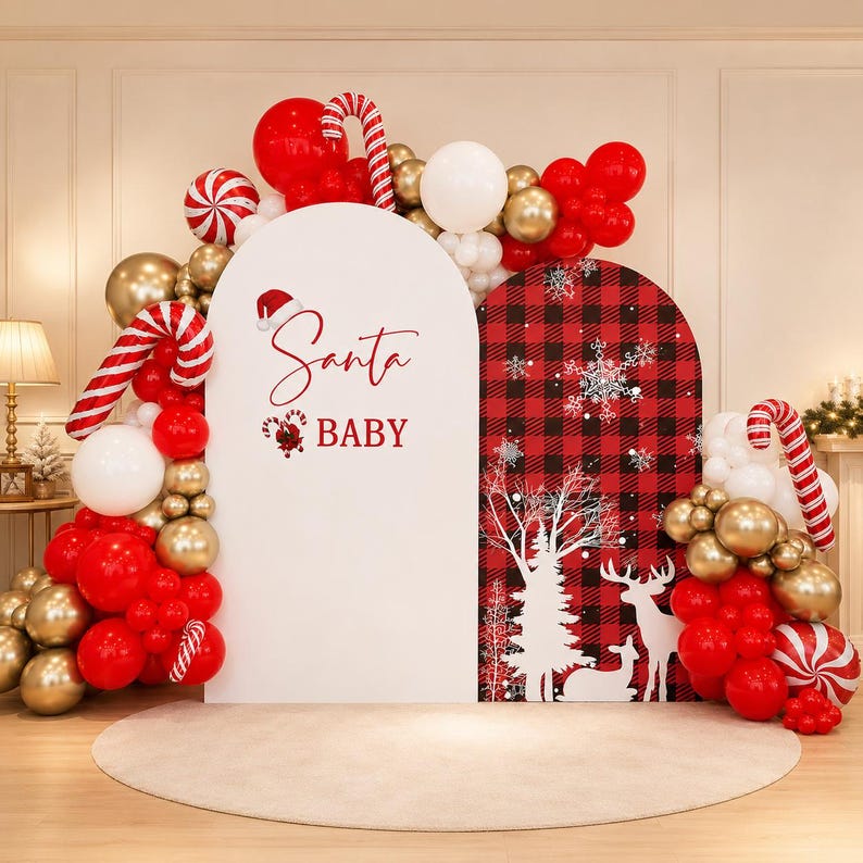 May include: A Christmas-themed party backdrop featuring two arched panels, one white with the red text Santa BABY and a candy cane graphic, and one with a red and black buffalo plaid pattern, white trees, and deer, surrounded by red, white, and gold balloons.