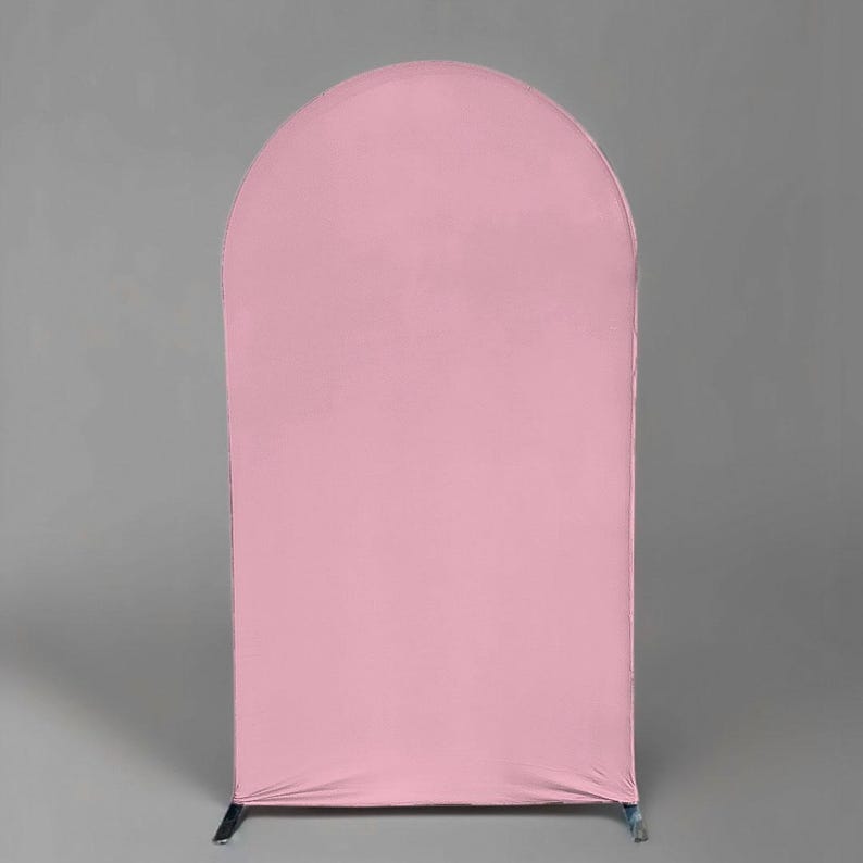 May include: A tall, arched backdrop stand covered in a smooth, solid light pink fabric cover. The structure features a rounded top edge and straight vertical sides, creating a clean, uniform surface that extends down to the base feet.