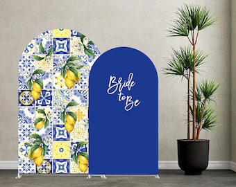 May include: Two arched backdrop covers. One features a blue and yellow Mediterranean tile pattern with yellow lemon illustrations. The other is solid blue with the white cursive text Bride to Be printed in the center of the arch.