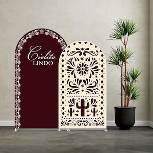 May include: Two arched backdrop panels. One is burgundy with the words "Cielito Lindo" in white script. The other is cream-colored with a cut-out floral and cactus design in burgundy. A potted plant is to the right.
