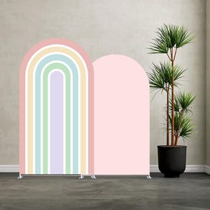 Könnte beinhalten: Zwei gewölbte Hintergrundpaneele. Ein Panel zeigt ein Regenbogenmuster mit Pastellfarben, darunter Rosa, Gelb, Blau und Grün. Das andere Panel ist einfarbig rosa. Eine Topfpflanze mit grünen Blättern befindet sich im Hintergrund.