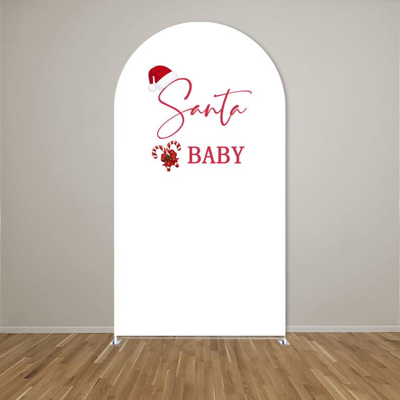 May include: A white arched backdrop cover featuring a red Santa hat graphic above the red cursive text Santa and the block text BABY, accompanied by a red and white candy cane illustration with a green holly accent on the left side.