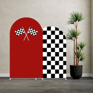 May include: Two arched backdrop panels. One is solid red with crossed checkered flags. The other is a black and white checkered pattern. A potted plant is to the right of the panels. The panels are on a gray floor.
