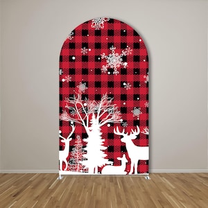 May include: An arched backdrop cover featuring a red and black buffalo plaid pattern. The design includes white silhouettes of deer, a large pine tree, and various snowflake shapes scattered across the surface, creating a winter-themed display.