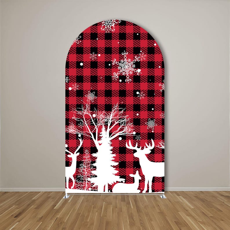May include: An arched backdrop cover featuring a red and black buffalo plaid pattern. The design includes white silhouettes of deer, a large pine tree, and various snowflake shapes scattered across the surface, creating a winter-themed display.