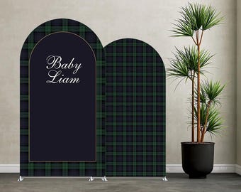May include: A navy blue and green plaid backdrop with an arched design. The backdrop features the text "Baby Liam" in elegant script within a navy blue frame. A potted plant is to the right.