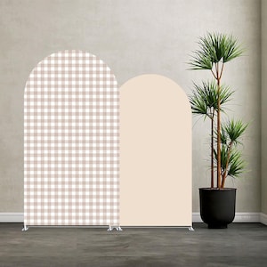 May include: Two arched backdrop panels. One panel has a tan and white gingham pattern, the other is a solid light peach colour. The panels are supported by a silver metal frame. A potted plant with green leaves is to the right.