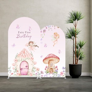 Puede incluir: Dos paneles de fondo arqueados con un fondo rosa claro e ilustraciones en acuarela de hadas, una casa de hongos, flores y mariposas. El texto "Fairy First Birthday" está impreso en letra cursiva marrón en el panel izquierdo.