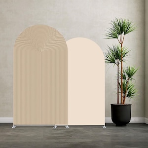 Könnte beinhalten: Zwei bogenförmige Raumteiler. Einer ist beige mit vertikalen Linien und einer gewölbten Oberseite. Der andere ist einfarbig hellpfirsichfarben. Rechts von den Trennwänden befindet sich eine hohe Topfpflanze mit grünen Blättern.
