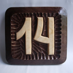 May include: A wooden plaque with a carved number "14" in a light wood color. The plaque is dark brown with a decorative border.
