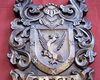 May include: A wooden carved coat of arms with a crest and a shield featuring a bird. The shield is surrounded by ornate scrollwork. The name "GARCIA" is carved on a banner below the shield.