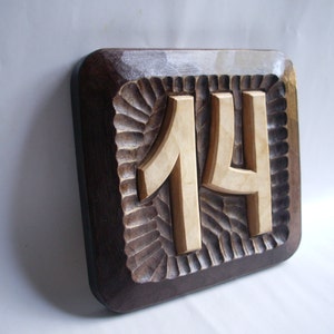 May include: A wooden house number plaque with the number 14 carved into it. The plaque is dark brown with a light brown border and a carved design around the number.