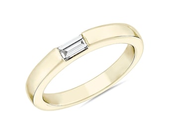 May include: A polished yellow gold band ring featuring a single, clear, rectangular baguette-cut diamond set horizontally into the center of the metal band. The ring has a smooth, rounded profile and a high-shine metallic finish throughout.