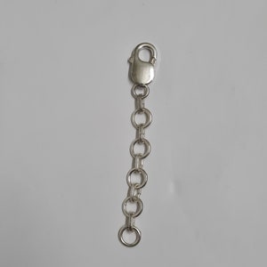 Puede incluir: Una cadena extensora de joyer&iacute;a de metal plateado que presenta una serie de cinco eslabones circulares conectados a un cierre de mosquet&oacute;n en un extremo. La cadena est&aacute; compuesta por componentes met&aacute;licos pulidos y reflectantes.