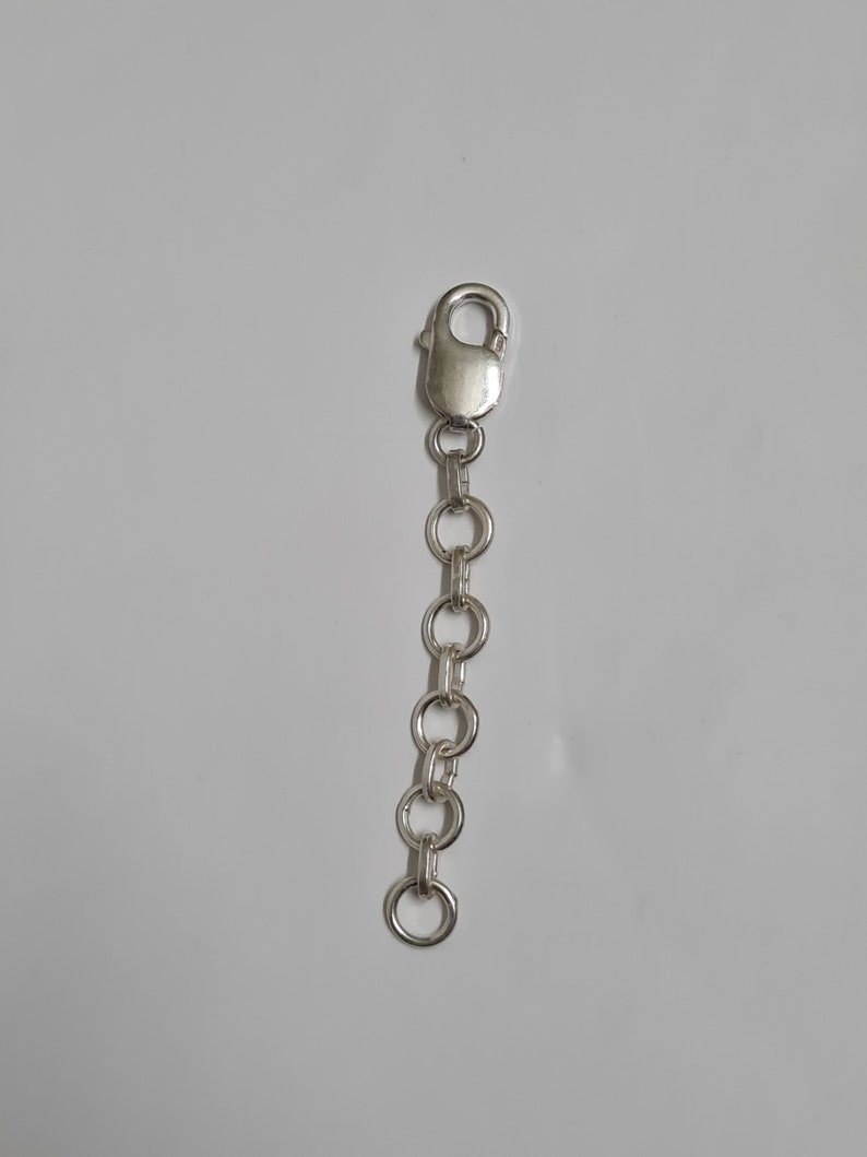Puede incluir: Una cadena extensora de joyer&iacute;a de metal plateado que presenta una serie de cinco eslabones circulares conectados a un cierre de mosquet&oacute;n en un extremo. La cadena est&aacute; compuesta por componentes met&aacute;licos pulidos y reflectantes.